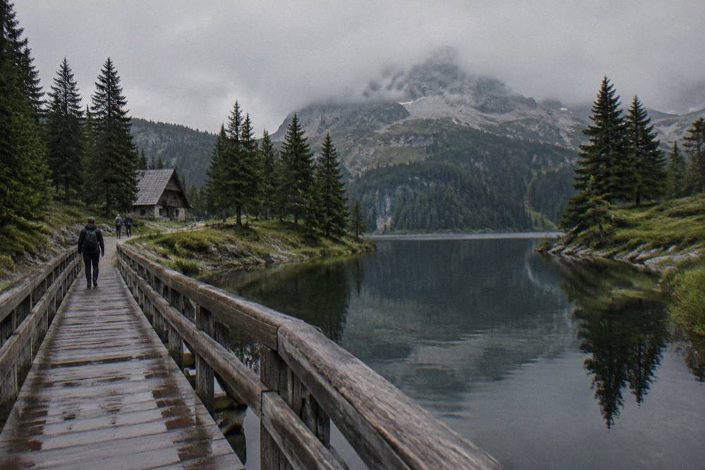 Dark still water of a mountain lake with pine trees reflected and a rocky peak behind