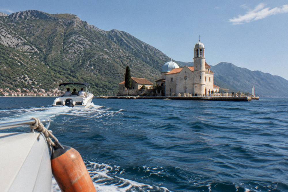 A speedboat crossing turquoise water toward a stone island with a chapel on it